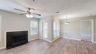 Located at 2696 N Druid Hills Rd NE in Atlanta, Georgia, this single-floor residence offers a well-designed layout with a comfortable, functional interior throughout. The open living and dining area is finished with wood-look flooring and neutral gray walls, creating a bright and welcoming atmosphere. A black-surround fireplace serves as a focal point in the living room, complemented by multiple windows dressed with white blinds that invite natural light. A ceiling fan with a light fixture adds both practicality and comfort to the space. The adjoining dining area features a pendant light fixture and a chair rail detail along the wall. The kitchen is equipped with dark cabinetry, granite-style countertops, stainless steel appliances including a refrigerator, microwave, and electric range, and wood-look flooring that carries through from the main living area. A breakfast bar provides a seamless connection between the kitchen and living space. The bedrooms are carpeted for comfort, each featuring ceiling fans and generous natural light. One bedroom includes sliding glass doors that open to a private balcony overlooking lush greenery. The bathroom is finished with a tiled tub-shower combination, a framed mirror, and clean, neutral finishes throughout.