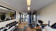 This single-floor fitness center at 2770–2798 Teagu in Houston, Texas offers a well-equipped workout facility designed to meet a range of exercise needs. The space is divided into distinct functional zones, seamlessly connected through glass-paneled sliding doors that enhance the open feel of the interior. Flooring throughout consists of durable parquet-style wood tile, and the textured ceilings feature recessed panel lighting that keeps the space bright and functional.

The cardio area is equipped with a treadmill, elliptical trainer, and stationary bike, all positioned near large windows that provide views of the surrounding outdoor pool area, allowing natural light to fill the space during workouts. A wall-mounted flat-screen television is conveniently located nearby, and a standing fan provides additional airflow.

The strength training section houses a multi-functional cable machine, a dumbbell rack with a full set of free weights, and a weight bench. Full-length mirrors are mounted along the walls, visually expanding the space and allowing users to monitor their form. A dedicated fitness center rules sign is posted, reflecting an organized and community-focused environment.

Large sliding glass doors open directly to an outdoor terrace and pool deck, providing easy indoor-outdoor access and a refreshing connection to the exterior amenities. Overall, the fitness center offers a compact yet comprehensive environment for daily exercise.