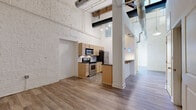 Unit 423 at 113-121 N 20th St in Richmond, VA is a thoughtfully designed studio-style unit that blends industrial character with modern updates. The living area immediately impresses with soaring ceilings, whitewashed exposed brick walls, and original heavy timber beams that speak to the building's historic roots. Warm-toned wood-style flooring runs throughout, and a classic white fireplace serves as a focal point, adding both charm and coziness to the space. The entry foyer is well-lit and welcoming, with clean white walls and an exposed beam accent that carries the industrial aesthetic seamlessly throughout. The kitchen is efficiently laid out and well-appointed, featuring light maple cabinetry, dark granite countertops, a tiled backsplash, and stainless steel appliances including a range, microwave, refrigerator, and dishwasher. Distinctive blue pendant lights hang above the kitchen counter, adding a modern, stylish touch. The bathroom is clean and functional, offering a vanity with matching dark countertop, a full tub-shower combo, and neutral tile flooring. A dedicated closet provides practical storage. This unit offers a compelling combination of historic architectural detail and contemporary finishes in a compact, well-organized layout.