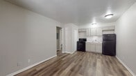 This single-floor unit offers a clean, modern layout designed for efficient, comfortable living. The open-concept main area seamlessly connects the living space to the kitchen, creating a functional and airy feel. The kitchen is well-equipped with grey shaker-style cabinetry extending to the ceiling for ample storage, a white subway tile backsplash, a double-basin sink, and a full suite of black appliances including an electric range and refrigerator. Durable wood-look flooring runs consistently throughout the entire unit, providing a cohesive and easy-to-maintain surface in every room. The bedroom is a quiet, well-proportioned room featuring a window with blinds that allows for natural light while maintaining privacy. Neutral grey tones on the walls complement the flooring, creating a calm and versatile aesthetic. The bathroom is straightforward and functional, offering a walk-in shower stall, a toilet, and a vanity with sink. Textured walls in the bathroom add a subtle design contrast to the otherwise smooth finishes found throughout the rest of the unit. The overall design of this space prioritizes clean lines, neutral tones, and practical finishes, making it a move-in-ready option suited to a variety of living needs.