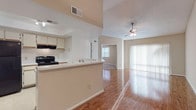 This single-story residence is defined by its striking vaulted ceilings in the main living area, which lend an airy, expansive quality to the open-concept floor plan. Warm hardwood-style flooring flows throughout the living and dining spaces, reflecting natural light that enters generously through large sliding glass doors fitted with vertical blinds. A ceiling fan overhead complements the sense of comfort and openness.

The kitchen is positioned adjacent to the living area and features a peninsula counter that serves as a natural divider between the two spaces. Cream cabinetry, a black electric range, a black refrigerator, and a recessed tray ceiling with track lighting give the kitchen a functional and tidy character. A sink along the peninsula adds convenience for both cooking and entertaining.

The bedrooms are carpeted and offer a quieter, softer atmosphere. One bedroom includes dual closets with louvered bifold doors and a ceiling fan, while another features direct sliding glass door access to the outdoors, filling the room with natural light and exterior views. An en suite bathroom connects to one of the bedrooms, complete with a vanity topped in stone-look counters.

Two bathrooms serve the residence — one with a tub-shower combination and tile surround, and another with a dedicated walk-in shower and white tile walls, both finished with clean, neutral tones throughout.