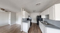 This 2-bedroom, 1-bathroom unit offers a practical and efficient single-floor layout. The galley-style kitchen is well-appointed with white cabinetry, gray laminate countertops, a stainless steel double sink, a black gas range, and a black refrigerator. A textured ceiling and dark wood-look vinyl flooring run throughout, providing a consistent aesthetic across the space. Adjacent to the kitchen, a dining or entry area benefits from a window that brings in natural light and provides access to the front door.

Both bedrooms feature the same wood-look flooring, neutral gray walls, ceiling fans with integrated lighting, and windows fitted with blinds for natural light and privacy. Each room also includes dedicated closet space, adding practical storage to the layout.

The bathroom is equipped with a white vanity featuring gray countertops, a toilet, and a full-size tub and shower combination with clean white surround walls. Dark wood-look flooring continues into this space, maintaining a cohesive look throughout the unit.

Overall, the unit presents a clean, functional design with consistent finishes, making efficient use of its compact footprint across all rooms.