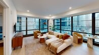 Located in the heart of Philadelphia at 1701 Market St, this modern 2-bedroom, 2-bathroom residence offers a thoughtfully designed single-floor layout. The open-plan kitchen and living area is a standout, featuring floor-to-ceiling windows that frame sweeping views of the Philadelphia skyline, flooding the space with natural light. The kitchen is appointed with white upper cabinetry, warm wood lower cabinets, a marble-style backsplash, stainless steel appliances, and a generous white quartz waterfall island with bar seating illuminated by globe pendant lights in brass.

The living area extends naturally from the kitchen, with expansive black-framed windows offering a panoramic urban backdrop. Both bedrooms are well-proportioned and serene, with light hardwood flooring and ceiling fans. The primary bedroom benefits from a custom open closet system featuring black metal frames, white shelving, built-in drawers, and multiple hanging sections for organized storage.

The bathrooms are finished to a high standard, with one showcasing a wood-toned floating vanity, white quartz countertop, backlit mirror, gold hardware, and large-format marble-style shower tiles. Additional features include a dedicated laundry area, multiple closets, and a welcoming entrance foyer — all combining to create a polished, contemporary urban residence.