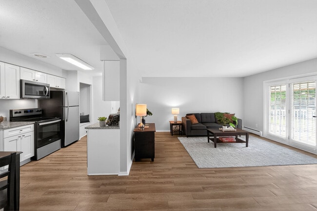 Contemporary open-plan kitchen and living room with sleek appliances, hardwood floors, and abundant natural light. - University Oaks
