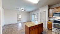 This well-designed one-bedroom, one-bathroom unit in White Settlement, TX offers a functional and comfortable layout across a single floor. The open-concept living and kitchen area serves as the heart of the home, anchored by a central island topped with granite countertops that provides additional prep space and casual dining. The kitchen is outfitted with rich wood cabinetry, stainless steel appliances including a refrigerator, dishwasher, range, and microwave, and consistent granite surfaces that tie the space together. Durable hardwood-style flooring runs throughout the main living areas, complemented by a ceiling fan overhead. Sliding glass doors lead to a private balcony, allowing natural light to fill the living space and offering outdoor views. The bedroom features plush carpeting, a ceiling fan, and a window that brings in additional natural light. It connects directly to a dedicated closet and the full bathroom, which mirrors the kitchen's design with matching wood cabinetry, granite countertops, and a tub-shower combination. The consistent finishes throughout the unit create a cohesive and practical living environment.