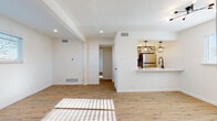 This single-floor space offers a clean, contemporary design highlighted by light wood-toned flooring, crisp white walls, and abundant natural light throughout. The open living area is spacious and airy, featuring recessed lighting, a structural ceiling beam detail, and a pass-through breakfast bar that connects seamlessly to the kitchen. The kitchen is well-equipped with stainless steel appliances, including a refrigerator, electric range, and over-the-range microwave, complemented by white shaker-style cabinetry, white subway tile backsplash, light countertops, and matte black pendant lighting that adds a modern industrial touch. The bedroom is a comfortable retreat with warm wood flooring, a ceiling fan with a light fixture, and a window that allows natural light to filter in. The bathroom is tastefully updated with gray subway tile surrounding a full soaking tub and shower, matte black fixtures and hardware, a white vanity with a round mirror, and wood-look flooring that ties the space together. Throughout the unit, consistent flooring, neutral tones, and modern finishes create a cohesive and inviting atmosphere well-suited for everyday living.