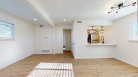 This single-floor space offers a clean, contemporary design highlighted by light wood-toned flooring, crisp white walls, and abundant natural light throughout. The open living area is spacious and airy, featuring recessed lighting, a structural ceiling beam detail, and a pass-through breakfast bar that connects seamlessly to the kitchen. The kitchen is well-equipped with stainless steel appliances, including a refrigerator, electric range, and over-the-range microwave, complemented by white shaker-style cabinetry, white subway tile backsplash, light countertops, and matte black pendant lighting that adds a modern industrial touch. The bedroom is a comfortable retreat with warm wood flooring, a ceiling fan with a light fixture, and a window that allows natural light to filter in. The bathroom is tastefully updated with gray subway tile surrounding a full soaking tub and shower, matte black fixtures and hardware, a white vanity with a round mirror, and wood-look flooring that ties the space together. Throughout the unit, consistent flooring, neutral tones, and modern finishes create a cohesive and inviting atmosphere well-suited for everyday living.