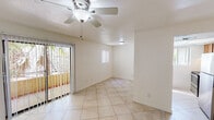 This single-floor residence offers a clean, well-organized layout with a light and airy feel throughout. The main living area is finished with large-format ceramic tile flooring set in a classic grid pattern, complemented by a textured ceiling and a ceiling fan with an integrated light fixture. A full-width sliding glass door opens to an outdoor area, allowing natural light to pour in and providing views of mature tropical landscaping. An additional window further brightens the space.

The kitchen features warm wood cabinetry, light-colored countertops, and includes a stainless electric range, a built-in microwave, and a refrigerator. A pass-through window connects the kitchen to the adjacent dining or utility area, enhancing the open feel of the layout. Nearby, a dedicated built-in shelving and storage closet offers practical organizational space.

The bedrooms are finished with the same tile flooring, neutral walls, and ceiling fans, with windows that frame views of the surrounding greenery. Both bathrooms are identically appointed with single-basin vanities featuring wood cabinetry, full-width mirrors, tub-shower combinations, and tile flooring, offering a clean and functional design. The overall palette of soft whites and warm neutrals gives this residence a calm, move-in ready atmosphere.
