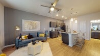 This thoughtfully designed single-floor residence offers a seamless open-concept layout that connects the living area and kitchen, creating a spacious and functional atmosphere. The living room features warm wood-look flooring, a ceiling fan with integrated lighting, and recessed lighting overhead, lending the space a bright and contemporary feel.

The kitchen is a standout feature, showcasing dark espresso-toned cabinetry that extends to the ceiling for ample storage, granite-style countertops, and a full suite of stainless steel appliances including a refrigerator, range, and built-in microwave. A peninsula with an under-mount sink and bar seating provides additional prep space and a natural divide between the kitchen and living areas. Pendant lighting above the peninsula adds a polished finishing touch.

The bedroom offers a relaxed retreat with plush carpeting, a ceiling fan, natural light from a window with blinds, and generous closet access. A second bedroom or flex room mirrors the same comfortable aesthetic.

The bathroom is finished with a dark wood vanity, granite countertop, a large framed mirror with lighted fixtures above, and a shower-tub combination, all set on wood-look flooring that ties the space together cohesively. Throughout, the consistent use of warm tones, modern fixtures, and quality finishes create an inviting and well-coordinated living environment.