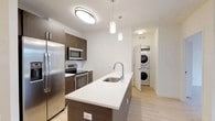 Located at 550 Halstead Ave in Harrison, NY, this well-appointed one-bedroom, one-bathroom residence offers a thoughtfully designed single-floor layout with modern finishes throughout. Light hardwood flooring flows seamlessly across the living, kitchen, and bedroom areas, creating a cohesive and bright aesthetic.

The open-concept kitchen is a standout feature, showcasing rich dark wood cabinetry, a large center island with a white quartz countertop and built-in sink, stainless steel appliances including a French door refrigerator, electric range, and microwave, along with pendant lighting that adds a contemporary touch. A dedicated in-unit laundry closet with a stacked washer and dryer is conveniently located just off the kitchen.

The spacious living area is bathed in natural light from oversized windows that frame outdoor views of the surrounding neighborhood. The bedroom is generously sized, featuring a large window with exterior views and a wide sliding-door closet for ample storage.

The bathroom is finished with floor-to-ceiling tiled walls in the shower/tub combo, a sleek dark-framed vanity with backlit mirror, and contemporary tile flooring. Clean white walls and flush-mount lighting throughout the home contribute to its bright, modern ambiance.