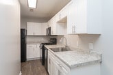 This single-floor residence on Vinegar Hill Drive in Greensboro, NC offers a thoughtfully arranged layout with neutral tones and consistent finishes throughout. The kitchen is a standout feature, outfitted with white shaker-style cabinetry, light granite-look countertops, a stainless steel sink, and black appliances including a gas range and refrigerator. Wood-look luxury vinyl flooring runs through the kitchen, providing both durability and visual warmth.

The living and bedroom areas are finished with plush, neutral-toned carpet that adds comfort underfoot. Multiple windows fitted with horizontal blinds allow natural light to filter into each room, creating a bright and airy atmosphere. The spacious bedroom includes two closets with built-in rods for ample storage, while additional carpeted rooms offer flexible use as bedrooms or living spaces.

The bathroom features a full tub-shower combination with white tile surround, chrome fixtures, a toilet, and a vanity with light countertops and white cabinetry, complemented by wood-look flooring. Crisp white trim and baseboards frame each room consistently throughout the unit. The overall design is clean and functional, offering a move-in-ready environment with practical finishes suited for everyday living.