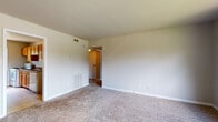 This single-story space is thoughtfully laid out to maximize functionality across its living areas. The living room is generously proportioned, featuring neutral-toned carpet, smooth walls with clean white baseboards, and a doorway opening directly toward the kitchen, creating a connected flow between the two spaces. A large window in the living area allows natural light to fill the room while offering views of the surrounding exterior.

The kitchen is well-equipped, featuring warm honey-toned wood cabinetry both above and below the countertops, a dark granite-style countertop, a stainless steel sink, and a white electric range. A sizable window above the counter brings in natural light and frames a view of mature trees outside.

The bedrooms are carpeted and finished in soft neutral tones, each benefiting from multiple windows that provide cross-ventilation and outdoor views. One bedroom includes a spacious open closet system with dual hanging rods and built-in shelving, offering notable storage capacity.

The bathroom is clean and functional, featuring tile flooring, a dark wood vanity with a granite-style countertop, a full tub-shower combination with a window above for natural light, and brushed nickel fixtures throughout. The overall ambiance of the space is simple, bright, and move-in ready.