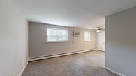 This single-floor, 2-bedroom, 1-bathroom residence offers a thoughtfully organized layout designed for comfortable everyday living. The spacious primary bedroom is the standout room, featuring wall-to-wall carpeting, multiple windows with blinds that invite natural light, a ceiling fan with a wall-mounted air conditioning unit for year-round climate control, and a large double bi-fold closet providing generous storage. The second bedroom maintains a similar carpeted aesthetic with its own window overlooking greenery and baseboard heating along the perimeter walls. The kitchen is efficiently designed with rich cherry wood cabinetry, granite-look countertops, a tile backsplash, and light hardwood-style flooring. It is equipped with a gas range, refrigerator, and a stainless steel sink, making it a fully functional cooking space. The bathroom is clean and bright, featuring a full tub-shower combination with white tile surround and chrome fixtures set atop neutral tile flooring. Neutral gray tones carry throughout the living areas, complemented by white trim and doors that give the space a cohesive, move-in-ready feel. Baseboard heating is present throughout, ensuring consistent warmth across all rooms.