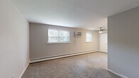 This single-floor, 2-bedroom, 1-bathroom residence offers a thoughtfully organized layout designed for comfortable everyday living. The spacious primary bedroom is the standout room, featuring wall-to-wall carpeting, multiple windows with blinds that invite natural light, a ceiling fan with a wall-mounted air conditioning unit for year-round climate control, and a large double bi-fold closet providing generous storage. The second bedroom maintains a similar carpeted aesthetic with its own window overlooking greenery and baseboard heating along the perimeter walls. The kitchen is efficiently designed with rich cherry wood cabinetry, granite-look countertops, a tile backsplash, and light hardwood-style flooring. It is equipped with a gas range, refrigerator, and a stainless steel sink, making it a fully functional cooking space. The bathroom is clean and bright, featuring a full tub-shower combination with white tile surround and chrome fixtures set atop neutral tile flooring. Neutral gray tones carry throughout the living areas, complemented by white trim and doors that give the space a cohesive, move-in-ready feel. Baseboard heating is present throughout, ensuring consistent warmth across all rooms.