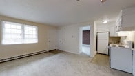 This single-floor 1-bedroom, 1-bathroom unit offers a practical and efficient layout well-suited for comfortable everyday living. The main living area features wall-to-wall carpeting and neutral, light-toned walls that create a clean, airy atmosphere. A window along the exterior wall allows natural light to filter into the space, while a baseboard heating unit ensures year-round comfort. The front entry door opens directly into this open living area, which connects seamlessly to the rest of the unit. A passageway leads to an additional space, where exposed brick detailing adds a touch of character and architectural warmth. The kitchen is positioned adjacent to the living area and features tile flooring, a full-size refrigerator, and ample room for essential appliances and cabinetry. The overall design is straightforward and functional, making efficient use of the available footprint. Neutral finishes and consistent lighting throughout the unit contribute to a cohesive, understated aesthetic. This unit is well-suited for those seeking a manageable, low-maintenance living space with a simple, practical floor plan.