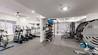 Located at 2900 Pharr Court South NW in Atlanta's prestigious Buckhead neighborhood, this well-equipped fitness center offers a comprehensive workout environment across a single floor. The space is finished with a clean, modern aesthetic, featuring crisp white walls accented by crown molding, recessed lighting, and ceiling fans that maintain a comfortable atmosphere throughout.

The cardio zone is dedicated to a row of treadmills and elliptical trainers positioned alongside windows that allow natural light and views of the surrounding exterior. A wall-mounted television provides entertainment during cardio sessions. An accent wall with a subtle wood-panel design adds a refined touch to this area.

The strength training section is equally well-appointed, housing a Cybex cable machine, a TRX suspension system, and a dedicated free weight area with a full rack of dumbbells, kettlebells, and medicine balls organized on a multi-tier storage rack. Additional equipment includes a rowing machine and a recumbent bike, catering to a variety of fitness routines.

Durable tile flooring with rubber mat overlays runs throughout, providing both safety and ease of maintenance. A water station is conveniently positioned near the entrance, and glass-paneled doors lead to adjoining common areas. The overall design is functional, clean, and thoughtfully organized to support a full range of fitness activities.