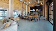 Located at 1744 Revere Beach Pkwy in Everett, MA, this striking single-floor commercial space masterfully blends industrial and natural design elements into a cohesive, open-concept environment. Soaring ceilings with exposed structural timber beams and warm wood-paneled walls create a sense of grand scale throughout, while polished concrete floors provide a clean, modern foundation that ties each zone together seamlessly.

The bar area serves as a focal point, featuring a substantial wood-topped island with black bar seating, statement pendant lighting, dual mounted televisions, and an extensive bottle display wall — all framed by floor-to-ceiling windows that flood the space with natural light and offer views of the surrounding exterior. Adjacent to the bar, a generous communal dining area accommodates long wooden tables lined with classic black spindle chairs, ideal for collaborative gatherings or shared meals.

A lounge zone offers a more intimate setting, anchored by a bold matte black accent wall with a built-in fireplace, rustic wooden coffee tables, and plush seating. The billiards room stands out with its dramatic double-height ceilings, warm wood walls, and floor-to-ceiling industrial shelving displaying an eclectic collection of globes and books, alongside a full-size pool table. Exposed ductwork and structural columns throughout lend an authentic industrial character to this thoughtfully designed, multifunctional space.