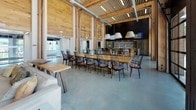 Located at 1744 Revere Beach Pkwy in Everett, MA, this striking single-floor commercial space masterfully blends industrial and natural design elements into a cohesive, open-concept environment. Soaring ceilings with exposed structural timber beams and warm wood-paneled walls create a sense of grand scale throughout, while polished concrete floors provide a clean, modern foundation that ties each zone together seamlessly.

The bar area serves as a focal point, featuring a substantial wood-topped island with black bar seating, statement pendant lighting, dual mounted televisions, and an extensive bottle display wall — all framed by floor-to-ceiling windows that flood the space with natural light and offer views of the surrounding exterior. Adjacent to the bar, a generous communal dining area accommodates long wooden tables lined with classic black spindle chairs, ideal for collaborative gatherings or shared meals.

A lounge zone offers a more intimate setting, anchored by a bold matte black accent wall with a built-in fireplace, rustic wooden coffee tables, and plush seating. The billiards room stands out with its dramatic double-height ceilings, warm wood walls, and floor-to-ceiling industrial shelving displaying an eclectic collection of globes and books, alongside a full-size pool table. Exposed ductwork and structural columns throughout lend an authentic industrial character to this thoughtfully designed, multifunctional space.