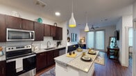 This single-story residence offers a thoughtfully designed open-concept layout where the kitchen flows seamlessly into the living area, creating a cohesive and functional living space. The kitchen is a standout feature, showcasing rich dark-wood cabinetry extending to the ceiling, granite countertops, a white subway tile backsplash, and a full suite of stainless steel appliances including a refrigerator, range, microwave, and dishwasher. A central island with granite countertops and stylish pendant lighting serves as both a prep area and casual dining space. Warm hardwood-style flooring runs throughout the unit, adding continuity and character.

The living area benefits from a ceiling fan and large glass French doors that invite natural light and provide outdoor access. The bedroom is a comfortable retreat featuring a ceiling fan, a large window with blinds and drape panels, and ample wall space. The bathroom includes granite countertops, dark wood cabinetry, and direct access to a dedicated laundry room equipped with a stacked Whirlpool washer and dryer alongside a built-in shelving rack, offering practical everyday convenience.