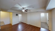 This single-floor unit offers a well-organized layout that flows naturally between its main living areas. The spacious main living room is finished with warm, rich hardwood-style flooring and features a tray ceiling detail with a ceiling fan and integrated light fixture. Multiple windows allow natural light to filter throughout the space, creating a bright and open ambiance. Cream-toned walls provide a neutral backdrop throughout, complemented by clean white baseboards and panel-style doors.

The kitchen is positioned adjacent to the living area and is defined by a raised breakfast bar with granite-style countertops, providing both workspace and a visual separation between rooms. Light wood cabinetry lines the walls and extends to the ceiling for ample storage, while black appliances, including a refrigerator, electric range, and microwave, add contrast. A stainless steel double-basin sink is integrated into the counter.

The bedroom features neutral carpet flooring, a window with a view, and a closet with panel-style doors. The bathroom is notably well-appointed, showcasing large-format dark brown tile surrounding a soaking tub and shower combination with sliding glass doors and a vessel-style sink vanity.