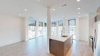 Located at 3000 Brighton Blvd in Denver's vibrant RiNo neighborhood, this modern 2-bedroom, 3-bathroom residence offers a thoughtfully designed open-concept layout with contemporary finishes throughout. The living and kitchen area is a true highlight, anchored by a sleek kitchen island with a waterfall countertop, dark walnut cabinetry, stainless steel appliances, and a built-in desk nook with open shelving. Floor-to-ceiling windows wrap the living space, flooding it with natural light and offering sweeping views of the Denver skyline and surrounding urban landscape. Light wood-style flooring flows throughout the main living areas, complementing the clean, minimalist aesthetic. A bright hallway with recessed lighting connects the living areas to the two bedrooms, each featuring plush carpeting, ceiling fans, and windows with city views. The spacious primary bedroom includes its own well-appointed en-suite bathroom with large-format tile flooring, a floating dark wood vanity with a white countertop, and a glass-enclosed shower. The additional bathrooms echo the same modern design sensibility. Two closets provide ample storage, completing this polished urban residence.