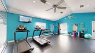 Located at 3440 N Goldenrod Rd in Winter Park, Florida, this fitness center offers a comprehensive workout environment within a single, efficiently utilized floor. The space is immediately recognizable by its bold teal accent walls, which lend an energetic and motivating ambiance throughout. Durable rubber flooring covers the entire area, providing a safe and functional surface suited to a wide range of exercise activities.

The main workout area is outfitted with multiple treadmills, elliptical trainers, stationary bikes, and a cable machine, offering a full suite of cardio and strength training options. A tiered dumbbell rack provides a varied selection of free weights, catering to users of all fitness levels. Wall-mounted flat-screen televisions are positioned for easy viewing during cardio sessions, enhancing the overall workout experience.

A separate spin studio is enclosed by frosted glass partitions, featuring additional stationary bikes in a dedicated, semi-private setting. Vaulted ceilings fitted with ceiling fans promote air circulation, while recessed lighting and natural light from multiple windows keep the space bright and well-ventilated. Mirrors along the walls further amplify the sense of openness. Accessories such as kettlebells, resistance bands, and exercise balls are also available, rounding out the facility's offerings.