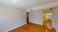 This single-floor home offers a clean, functional layout with consistent design details that create a cohesive and comfortable living environment. The main living area is defined by rich, warm-toned hardwood floors that extend throughout much of the space, complemented by crisp white crown molding and neutral-toned walls that provide a bright, open atmosphere. Ceiling-mounted HVAC vents reflect a well-integrated climate control system, and the layout flows naturally between the main rooms via open passageways.

The kitchen is a standout feature, showcasing white raised-panel cabinetry, dark granite-style countertops, and a stylish mosaic tile backsplash in shades of gray and blue. Black appliances, including a gas range, refrigerator, and built-in microwave, add a bold contrast, while recessed lighting and a window overlooking greenery keep the space bright and functional. A peninsula counter offers additional workspace and casual dining potential.

The bedroom benefits from natural light through a double-pane window with blinds, hardwood flooring, and a ceiling fan for comfort. The bathroom retains a classic character with white subway tile, a distinctive black tile accent border, a tub-shower combination, built-in shelving, and a window that introduces natural light. Together, these spaces form a well-appointed, move-in ready home.