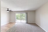 Located at 3606 S 50th St in Omaha, Nebraska, this single-floor unit offers a practical and comfortable layout across two bedrooms and two bathrooms. The galley-style kitchen is outfitted with white cabinetry, dark countertops, a stainless steel sink, and black appliances including a refrigerator and range, with light wood-look flooring that extends into the adjoining living area. The living room is a generously sized, open space featuring a modern ceiling fan with integrated lighting, neutral gray walls, and a mix of carpeted and hard-surface flooring that defines the transition between spaces. A sliding glass door allows natural light to filter into the living area. Both bedrooms are carpeted and finished with the same warm neutral tones, each featuring vertical-blind windows that bring in outdoor views of the surrounding greenery. The primary bedroom includes a closet with sliding doors, providing ample storage. The two bathrooms are clean and functional — one features a full soaking tub with a built-in surround shelf system and chrome fixtures, while the other is appointed with a towel bar and recessed paper holder. The overall aesthetic is understated and move-in ready, offering a cohesive, low-maintenance living environment.