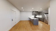 This well-designed single-story residence offers three bedrooms and two bathrooms within a thoughtfully laid-out floor plan. The open-concept kitchen and living area serves as the heart of the home, featuring a large peninsula with a white quartz countertop, an undermount sink, and sleek gray cabinetry extending to the ceiling. Stainless steel appliances, including a refrigerator, microwave, and range, complete the modern kitchen. Warm-toned hardwood flooring flows consistently throughout the entire space, complementing the clean white walls and recessed lighting overhead.

The primary bedroom offers a comfortable footprint with multiple windows that bring in natural light and views of surrounding greenery, along with a ceiling fan for added comfort. Additional bedrooms are well-proportioned with hardwood floors, individual heating units, and access to natural light. The two bathrooms are finished in a consistent modern style, each featuring gray vanity cabinetry, white countertops, and glass-enclosed showers.

A dedicated in-unit laundry room houses a full-sized top-loading washer and dryer with overhead shelving. Two closets provide practical storage throughout the home. The overall ambiance is clean, contemporary, and functional.