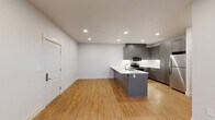 This well-designed single-story residence offers three bedrooms and two bathrooms within a thoughtfully laid-out floor plan. The open-concept kitchen and living area serves as the heart of the home, featuring a large peninsula with a white quartz countertop, an undermount sink, and sleek gray cabinetry extending to the ceiling. Stainless steel appliances, including a refrigerator, microwave, and range, complete the modern kitchen. Warm-toned hardwood flooring flows consistently throughout the entire space, complementing the clean white walls and recessed lighting overhead.

The primary bedroom offers a comfortable footprint with multiple windows that bring in natural light and views of surrounding greenery, along with a ceiling fan for added comfort. Additional bedrooms are well-proportioned with hardwood floors, individual heating units, and access to natural light. The two bathrooms are finished in a consistent modern style, each featuring gray vanity cabinetry, white countertops, and glass-enclosed showers.

A dedicated in-unit laundry room houses a full-sized top-loading washer and dryer with overhead shelving. Two closets provide practical storage throughout the home. The overall ambiance is clean, contemporary, and functional.