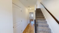 This three-floor home offers five bedrooms, three bathrooms, and a practical layout distributed across a compact but efficiently designed floor plan. The ground floor serves as an entry level, featuring a hallway with light hardwood flooring, a carpeted staircase with a wooden banister, and access to additional rooms. A half bathroom with hardwood flooring is also found on this level.

The main living floor hosts a combined dining and living area bathed in natural light from multiple windows, including a large sliding door dressed with vertical blinds. A ceiling fan with integrated lighting adds to the comfort of the space. The kitchen is well-equipped with dark espresso cabinetry, granite countertops, stainless steel appliances including a refrigerator, range, and microwave, complemented by light hardwood floors. A pantry provides additional storage adjacent to the kitchen.

The upper floor contains the bedrooms, including the primary bedroom, each featuring carpet flooring and closets with arched panel doors. The bathrooms are finished with granite-topped vanities, dark wood cabinetry, and clean white fixtures. Two staircases connect the floors throughout the home, contributing to a functional and accessible layout overall.