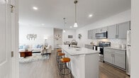 This thoughtfully designed single-floor residence offers 2 bedrooms and 2 bathrooms within a comfortable and functional layout. The open-concept living area seamlessly connects the kitchen, dining room, and living room, creating a bright and cohesive gathering space. Large sliding glass doors in the living room flood the area with natural light and are dressed with full-length vertical blinds. Recessed lighting and wood-look flooring run throughout, lending a clean, modern aesthetic.

The kitchen is a standout feature, boasting a large central island with granite countertops, pendant lighting, a stainless steel sink, and grey shaker-style cabinetry. Stainless steel appliances, including a range, microwave, and dishwasher, complete this functional culinary space. The adjacent dining area provides a comfortable setting for meals.

The primary bedroom is a well-proportioned retreat featuring a ceiling fan, natural window light, and access to a closet. The en-suite bathroom includes grey cabinetry with granite countertops and a glass-enclosed shower. The second bedroom is bright and inviting, with vertical blinds offering privacy. A dedicated laundry room houses a full-sized washer and dryer with overhead shelving, adding everyday convenience.