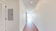Located in Nashville, TN, this efficiently designed single-floor unit offers a clean, contemporary aesthetic throughout. Rich hardwood flooring runs continuously across the open-concept layout, connecting the living area and kitchen in a cohesive, light-filled space. A bright hallway with recessed lighting and a ceiling fan leads into the main living area, where oversized windows frame sweeping elevated views of the Nashville skyline, surrounding neighborhoods, and distant mountain ridgelines, flooding the interior with abundant natural light.

The kitchen is well-appointed with a two-tone cabinetry design—white upper cabinets contrasted by warm wood-grain lower cabinets—complemented by light countertops and a vertically stacked gray tile backsplash. Stainless steel appliances, including a range, microwave, dishwasher, and refrigerator, complete the functional and stylish kitchen setup.

The bathroom features a full soaking tub with floor-to-ceiling dark tile surround in a vertical stacked pattern, accented by polished chrome fixtures, offering a sleek, modern finish. Throughout the unit, the crisp white walls and clean lines create a bright, minimalist ambiance well-suited to contemporary urban living in one of Nashville's vibrant neighborhoods.