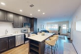 Located at 95 Newport Ave in East Providence, Rhode Island, this 1-bedroom, 1-bathroom residence is thoughtfully designed with a modern aesthetic and efficient single-floor layout. The open-concept kitchen and living area serves as the heart of the home, anchored by a striking kitchen featuring dark shaker-style cabinetry, white quartz countertops, stainless steel appliances — including a range, microwave, and dishwasher — and a large center island with bar seating, ideal for dining and entertaining. The kitchen flows seamlessly into the living room, which is bathed in natural light from multiple windows and a glass-panel exterior door, creating a bright and welcoming atmosphere. Hardwood-style flooring runs throughout the main living areas, adding warmth and continuity. The bedroom offers plush carpeting, a generous window with exterior views, and a calm, neutral palette. The bathroom is finished with classic black-and-white mosaic tile flooring, a dark vanity with a white countertop, a large mirror, and a shower-tub combination. A dedicated laundry room with a stacked washer and dryer provides added convenience. Recessed lighting throughout completes the clean, contemporary feel of this well-designed residence.
