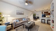 This single-floor residence offers a thoughtfully designed open-concept layout that seamlessly connects the living, dining, and kitchen areas. The living room features neutral-toned carpet, a ceiling fan, and generous wall space accented by framed artwork, creating a warm and inviting atmosphere. A glass-top coffee table and plush seating anchor the space, while natural light filters in through large windows dressed with sheer curtains.

The kitchen is outfitted with rich dark wood cabinetry, granite countertops, black appliances including a refrigerator, range, and microwave, and a peninsula with pendant lighting and bar seating. Light tile flooring extends throughout the kitchen and connects it cleanly to the adjacent dining area, which features track lighting overhead.

The bedroom is a comfortable retreat with plush carpeting, a ceiling fan, and French doors that allow natural light to fill the room. A built-in desk nook with shelving provides a dedicated workspace, while a spacious walk-in closet offers substantial storage. The full bathroom features tile flooring, dark wood vanity cabinetry, a granite countertop, and an arched alcove housing a soaking tub with shower combination, providing a clean and functional design.