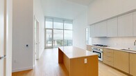This modern high-rise unit in San Diego, CA offers a sleek, contemporary design characterized by clean lines, light hardwood flooring, and soaring ceilings that amplify the sense of openness throughout. Floor-to-ceiling glass walls flood the interior with natural light and frame sweeping panoramic views of the San Diego skyline, Balboa Park, and the surrounding mountains.

The open-concept kitchen and living area is a standout feature, showcasing a large central island with a quartz countertop, warm wood cabinetry, stainless steel appliances including a gas range and built-in oven, and high-gloss upper cabinets that extend toward the tall ceilings for ample storage.

Both bedrooms feature expansive floor-to-ceiling windows with direct access to outdoor views, offering a bright and airy atmosphere. The generously sized primary bedroom includes built-in closet storage with glass-door shelving. The additional bedroom also benefits from abundant natural light and closet access.

The unit includes four well-appointed bathrooms, each finished with large-format floor tiles, wall-mounted toilets, floating wood-toned vanities, and backlit mirrors. One bathroom features a full soaking tub with textured tile surround.

A private balcony with glass railings offers unobstructed views, completing this refined urban retreat.