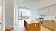 This modern high-rise unit in San Diego, CA offers a sleek, contemporary design characterized by clean lines, light hardwood flooring, and soaring ceilings that amplify the sense of openness throughout. Floor-to-ceiling glass walls flood the interior with natural light and frame sweeping panoramic views of the San Diego skyline, Balboa Park, and the surrounding mountains.

The open-concept kitchen and living area is a standout feature, showcasing a large central island with a quartz countertop, warm wood cabinetry, stainless steel appliances including a gas range and built-in oven, and high-gloss upper cabinets that extend toward the tall ceilings for ample storage.

Both bedrooms feature expansive floor-to-ceiling windows with direct access to outdoor views, offering a bright and airy atmosphere. The generously sized primary bedroom includes built-in closet storage with glass-door shelving. The additional bedroom also benefits from abundant natural light and closet access.

The unit includes four well-appointed bathrooms, each finished with large-format floor tiles, wall-mounted toilets, floating wood-toned vanities, and backlit mirrors. One bathroom features a full soaking tub with textured tile surround.

A private balcony with glass railings offers unobstructed views, completing this refined urban retreat.