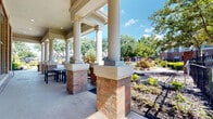 This two-story residential community is thoughtfully designed to blend classic architectural character with expansive outdoor amenities. The exterior showcases brick construction accented by ornamental ironwork fencing, decorative lamp posts, and stone-accented retaining walls that lend a refined, traditional aesthetic throughout the grounds.

At the heart of the outdoor space lies a generously sized resort-style swimming pool with a freeform design, complemented by a spacious sundeck lined with lounge chairs and patio umbrellas — ideal for relaxation under open skies. Adjacent to the pool, a stately covered pavilion features tall columnar pillars rising from brick bases, providing a shaded seating area furnished with tables and chairs.

The landscaping throughout the community is carefully curated, featuring vibrant shrubs, seasonal plantings, decorative rock beds, and mature shade trees that create a lush, park-like atmosphere. Winding flagstone and concrete pathways connect various outdoor seating areas, including a charming gazebo and a casual lounge area with patterned accent chairs arranged around a central courtyard.

A gated entry with brick pillar accents and ornamental iron fencing frames the community's perimeter, reinforcing its sense of privacy and security. The combination of well-maintained greenery, architectural detail, and abundant outdoor living spaces gives this community a welcoming and resort-inspired ambiance year-round.