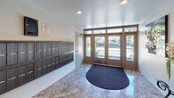 Located at 17830 Merridy St in the Northridge neighborhood of Los Angeles, this building lobby serves as a welcoming and functional entry point for residents and visitors alike. The space is finished with polished stone-style tile flooring in warm earth tones that reflects the recessed lighting overhead, lending the area a clean and polished appearance throughout.

Upon entry through the wide, glass-paneled double doors — framed with transom windows that draw in abundant natural light from the exterior — visitors are greeted by a spacious, open lobby. A large semi-circular entry mat anchors the entryway, providing a practical transition from outside. To one side of the entrance, a substantial bank of individual resident mailboxes is mounted along the wall, offering convenient mail access for all building occupants.

Moving deeper into the lobby, the space opens into a well-lit corridor leading to an elevator, providing access to the building's upper levels. The walls are decorated with framed artwork, adding a touch of character to the otherwise neutral, light-toned interior. Recessed ceiling lights illuminate the space evenly throughout. A small accent table with decorative detailing and a slim waste receptacle round out the lobby's furnishings, maintaining an organized and tidy atmosphere. Overall, the lobby presents a functional, clean, and welcoming communal space.
