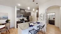 This single-floor residence is thoughtfully designed with a cohesive modern aesthetic throughout, characterized by crisp white walls, light wood-style flooring, and dark espresso cabinetry that creates a striking contrast across multiple rooms.

The kitchen is a central highlight, offering generous counter space finished in speckled granite, dark shaker-style cabinetry with brushed nickel hardware, and a full suite of stainless steel appliances including a refrigerator, range, microwave, and dishwasher. A kitchen island with an undermount sink and pendant lighting above provides additional prep space and casual seating. An adjacent dining nook offers an intimate setting conveniently positioned next to the kitchen.

The living area features recessed lighting and a set of glass doors that open to a private balcony, allowing natural light to filter in and providing views of the surrounding exterior.

The bedrooms are carpeted for comfort, with one featuring direct access to an en suite bathroom and a walk-in closet with wire shelving. The bathrooms maintain the home's consistent design language, each featuring granite-topped dark vanities, framed mirrors, and tile-surround tub-shower combinations. Light wood flooring extends through the bathrooms, tying the space together cohesively throughout.