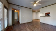 This single-story, two-bedroom, two-bathroom residence offers a functional and cohesive layout with consistent wood-style flooring flowing throughout the home. The living area serves as the central gathering space, featuring crown molding, a ceiling fan with light fixture, and a large window alongside a glass door that invites natural light and provides access to the outdoors. The kitchen is positioned adjacent to the living area with a pass-through counter, rich dark-toned cabinetry, granite-style countertops, and a full suite of black appliances including a refrigerator, range, and dishwasher. A dedicated corridor leads to both bedrooms, each equipped with a ceiling fan, neutral walls, and windows that allow natural light. The two bathrooms mirror each other in design, featuring warm wood-toned cabinetry, granite-style countertops, wood-style flooring, and a tub-shower combination with white tile surround. A dedicated in-unit laundry closet with wire shelving houses a full-size washer and dryer. Throughout the home, neutral tones, crown molding, and consistent finishes contribute to a clean, cohesive aesthetic.
