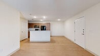 This thoughtfully laid-out 2-bedroom, 2-bathroom residence offers a cohesive single-floor plan with a clean, modern aesthetic. The open-concept living and kitchen area serves as the heart of the home, where light wood-tone flooring flows seamlessly throughout, creating a bright and airy atmosphere. Recessed lighting illuminates the space from above, enhancing the crisp white walls and clean lines.

The kitchen is a functional highlight, featuring warm wood-grain cabinetry extending to the upper walls, a granite-topped center island with an integrated sink, and a full suite of black appliances including a range, microwave, and refrigerator. The island provides both prep space and a natural divider between the kitchen and living room.

Both bedrooms offer comfortable proportions, with the primary bedroom providing a generous footprint. The secondary bedroom includes a ceiling fan and a window that brings in natural light and outdoor views. Two closets offer practical storage solutions throughout the unit.

The bathrooms are finished with elegant marble-style wall tiling surrounding deep soaking tubs, adding a refined touch to the overall design. A connecting hallway links the private and shared areas of the home efficiently. The consistent use of light flooring, neutral walls, and modern fixtures gives the entire space a cohesive and contemporary feel.