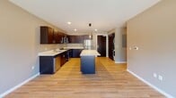 This thoughtfully designed single-floor residence offers a cohesive blend of modern finishes and functional living spaces. The kitchen serves as the heart of the home, featuring rich dark cabinetry, crisp white countertops, a central island ideal for casual dining or meal prep, and a full suite of stainless steel appliances including a refrigerator, range, microwave, and dishwasher. Light wood-tone flooring runs throughout the kitchen and common areas, lending warmth and continuity to the space. In-unit laundry is conveniently tucked nearby, adding to the overall practicality of the layout. The bedrooms are carpeted in a neutral blue-gray tone and benefit from abundant natural light through large windows fitted with roller shades. Ceiling fans provide comfortable airflow, and generous closet space with built-in shelving and hanging rods is featured in at least one bedroom. The bathrooms are finished with the same dark cabinetry as the kitchen, complemented by light wood-tone flooring, large vanity mirrors, and clean white fixtures. One bathroom features a combined tub and shower, while a second bathroom is visible nearby, offering added convenience. Neutral taupe wall tones throughout the residence create a calm, versatile backdrop ready for personalization.