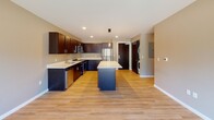 This thoughtfully designed single-floor residence offers a cohesive blend of modern finishes and functional living spaces. The kitchen serves as the heart of the home, featuring rich dark cabinetry, crisp white countertops, a central island ideal for casual dining or meal prep, and a full suite of stainless steel appliances including a refrigerator, range, microwave, and dishwasher. Light wood-tone flooring runs throughout the kitchen and common areas, lending warmth and continuity to the space. In-unit laundry is conveniently tucked nearby, adding to the overall practicality of the layout. The bedrooms are carpeted in a neutral blue-gray tone and benefit from abundant natural light through large windows fitted with roller shades. Ceiling fans provide comfortable airflow, and generous closet space with built-in shelving and hanging rods is featured in at least one bedroom. The bathrooms are finished with the same dark cabinetry as the kitchen, complemented by light wood-tone flooring, large vanity mirrors, and clean white fixtures. One bathroom features a combined tub and shower, while a second bathroom is visible nearby, offering added convenience. Neutral taupe wall tones throughout the residence create a calm, versatile backdrop ready for personalization.