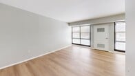 Located at 1321 Veterans Hwy in Bristol, PA, this single-floor, one-bedroom, one-bathroom residence offers a clean, modern aesthetic with consistent light wood flooring and neutral gray tones throughout. The open-concept kitchen and living area forms the heart of the unit, with the living room benefiting from a large, floor-to-ceiling window array fitted with horizontal blinds that invite generous natural light and outdoor views. The kitchen is well-appointed with white shaker-style cabinetry, marble-look countertops, stainless steel appliances including a gas range and full-size refrigerator, and a stainless steel sink — providing a functional and stylish cooking space. The bedroom is a comfortable, well-proportioned retreat featuring its own large window for natural light and an expansive built-in closet system with floor-to-ceiling white panel doors offering ample storage. The bathroom is straightforward and practical, equipped with a full-size soaking tub and shower combination with chrome fixtures and a curved curtain rod. Clean white walls and bright trim are consistent throughout, lending the space a fresh, move-in ready feel. The overall ambiance is light, airy, and modern — ideal for efficient, comfortable everyday living.