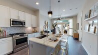 This single-floor residence showcases a thoughtfully designed open-concept layout that seamlessly connects the kitchen, dining, and living areas. The kitchen is a standout feature, equipped with stainless steel appliances, white shaker cabinetry, a decorative marble-style tile backsplash, and a large central island topped with a veined white quartz surface. Pendant lighting with glass and metal fixtures illuminates the island, which offers bar seating and serves as a natural gathering point. The living area benefits from large windows and glass door access to an outdoor space, filling the room with natural light and providing exterior views.

The entryway includes a built-in mudroom bench with open shelving, offering practical storage from the moment you arrive. The bedroom features floor-to-ceiling windows with outdoor views, a bold deep teal accent wall, and plush carpeting, creating a cozy yet sophisticated retreat. The bathroom is finished with herringbone tile flooring, gray cabinetry with quartz countertops, and a tiled tub-shower combination. Rich hardwood-style flooring runs throughout the main living areas, unifying the space with a warm, contemporary aesthetic.