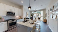 This single-floor residence showcases a thoughtfully designed open-concept layout that seamlessly connects the kitchen, dining, and living areas. The kitchen is a standout feature, equipped with stainless steel appliances, white shaker cabinetry, a decorative marble-style tile backsplash, and a large central island topped with a veined white quartz surface. Pendant lighting with glass and metal fixtures illuminates the island, which offers bar seating and serves as a natural gathering point. The living area benefits from large windows and glass door access to an outdoor space, filling the room with natural light and providing exterior views.

The entryway includes a built-in mudroom bench with open shelving, offering practical storage from the moment you arrive. The bedroom features floor-to-ceiling windows with outdoor views, a bold deep teal accent wall, and plush carpeting, creating a cozy yet sophisticated retreat. The bathroom is finished with herringbone tile flooring, gray cabinetry with quartz countertops, and a tiled tub-shower combination. Rich hardwood-style flooring runs throughout the main living areas, unifying the space with a warm, contemporary aesthetic.