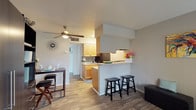 Located at 4210 Fredericksburg Rd in Balcones Heights, Texas, this single-floor unit offers a practical and well-organized layout ideal for comfortable everyday living. The open-concept design connects the living area and kitchen seamlessly, creating a cohesive and functional space throughout.

The living area features durable wood-look flooring that extends through the entire unit, neutral-toned walls, and a ceiling fan with integrated lighting that promotes consistent airflow and brightness. A window fitted with blinds allows natural light to filter into the living space while maintaining privacy.

The kitchen is a standout feature, centered around a peninsula breakfast bar with bar stool seating — ideal for casual dining or entertaining. Warm-toned wood cabinetry provides ample storage, complemented by a gray tile backsplash, light countertops, a stainless steel sink, and black appliances including a full-size refrigerator and stovetop range. A compact dining table adjacent to the kitchen adds additional meal and workspace options.

The bathroom is thoughtfully designed with a large framed mirror, a wood-cabinet vanity with light countertops, and a separate water closet with a toilet and shower area, offering a semi-divided layout for added convenience.

Overall, the unit presents a clean, cohesive aesthetic with warm wood tones and neutral finishes throughout.