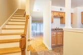 This two-floor residence offers a well-organized layout connected by a staircase that links both levels seamlessly. The main living area is finished with distinctive parquet wood flooring in a geometric pattern, lending a classic character to the space. Large vertical blinds cover a sliding glass door that invites natural light and provides access to an outdoor area. A pendant light fixture adds a focal point to the open dining and living zone, which also features a visible staircase leading to the upper floor.

The kitchen is equipped with stainless steel appliances, including a gas range, over-the-range microwave, refrigerator, and dishwasher. Warm honey-toned cabinetry provides ample storage, while a charming exposed brick backsplash adds a distinctive architectural detail. Tile flooring and a window with a blind complete the functional kitchen space.

The upper level features multiple rooms with rich hardwood flooring in varying tones. One room benefits from a window framing lush greenery, while another includes a built-in closet with a rod for organized storage. An additional room features lighter hardwood flooring with ceiling ventilation, offering a bright and airy feel throughout the upper floor.