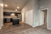 This single-floor residence is defined by its dramatic vaulted ceilings, which lend an expansive, airy quality to the open-concept living and kitchen area. Neutral gray walls and durable wood-look flooring run throughout the main living space, creating a cohesive and contemporary aesthetic.

The kitchen is a functional centerpiece, outfitted with rich dark cabinetry, crisp white countertops, and a full suite of stainless steel appliances including a range, microwave, dishwasher, and refrigerator. A freestanding island with a dark base and white countertop provides additional prep space and casual seating potential. Pendant lighting above the island and recessed ceiling lights ensure the kitchen is well-illuminated.

The living area benefits from the soaring ceiling height and includes a ceiling fan, adding to the sense of volume. A barn-style sliding door adds an architectural detail and leads to additional rooms. The bedroom features plush carpeting, a ceiling fan, and a window that brings in natural light. The walk-in closet connects directly to the full bathroom, which includes a tub/shower surround and tile flooring.